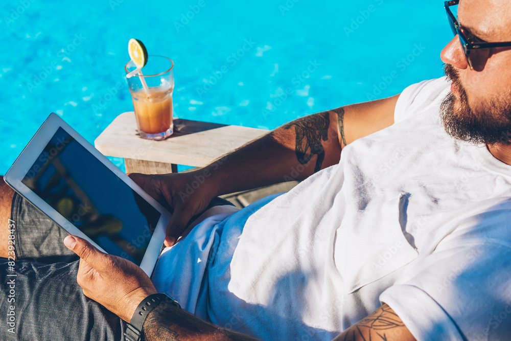 Poster bearded businessman in sunglasses resting on sunbed near blue pool enjoying summer time in luxury re