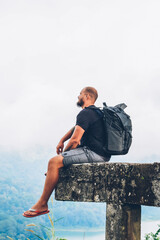 Dreamy bearded male tourist with travel backpack resting and admiring amazing high mountains...