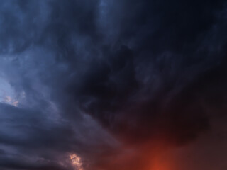 Ominous storm clouds fill the sky at dusk, contrasting with patches of orange light and intense...