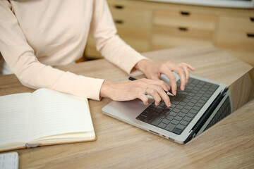 A woman is typing on a laptop in front of a notebook. She is wearing a ring on her finger