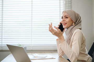 A woman wearing a hijab is talking on her cell phone. She is smiling and she is happy