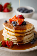 pouring syrup on piled pancake with strawberries and bluberries