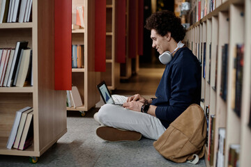 Side view of Middle Eastern male students sitting on floor in university library making...