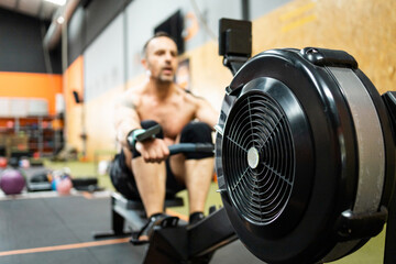 A middle-aged man is working out inside a gym.The 50-year-old is working on the lats with an air rowing machine.Concept of senior men in a gym.