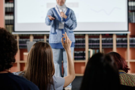 Selective focus shot of unrecognizable female student raising hand during lecture or conference in university library