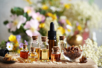 Bottles of aromatherapy essential oil with myrrh, frankincense and colorful spring flowers on a...