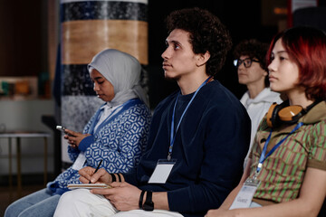 Selective focus shot of ethnically diverse male and female students sitting on chairs watching...