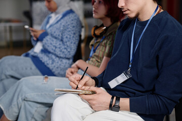 Selective focus shot of young Middle Eastern man writing notes in notebook at conference in...
