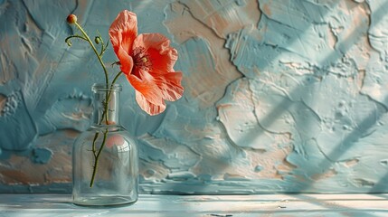   A solitary pink blossom graced a clear glass container positioned on top of a textured blue and pink backdrop