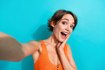 Portrait of ecstatic nice girl wear orange knit top making selfie palm on cheekbone staring open...