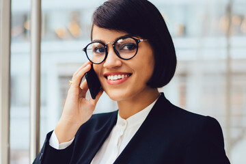 Portrait of cheerful female trader in eyeglasses satisfied with getting good financial news on...