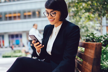 Female executive manager in elegant black suit resting on coffee break sending messages on...