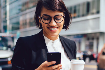 Smiling female owner reading funny message on smartphone while standing on street near...