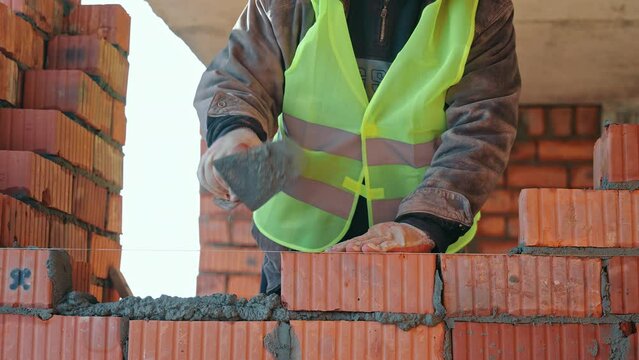 Close-up of Mortar Application on Brick Wall, Close-up of a construction worker's hands applying mortar on a brick wall, demonstrating precision in bricklaying techniques.