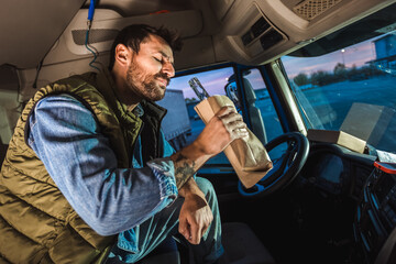 Young handsome man driving long vehicle, taking a break from long ride and drinking some alcohol.