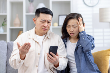 Concerned couple reacting to something on a smartphone screen, showing surprised and confused...
