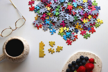 Colorful jigsaw puzzle pieces, cup of tea or coffee, eyeglasses and fresh berries for snacking....