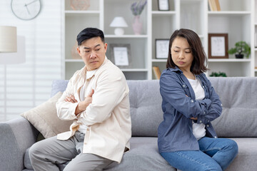 Couple in disagreement sitting apart on a sofa with arms crossed, depicting tension and unresolved...
