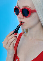 A beautiful woman paints her lips with red lipstick in sunglasses