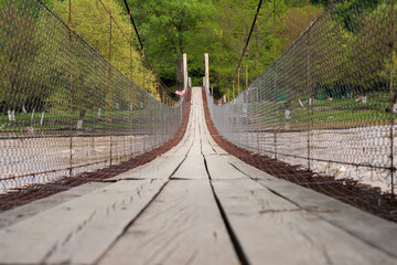 Footbridge with safety metal fence and wooden planks floor, hanging over the river on the green...