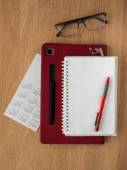 detail seen from above of a work table. Calendar, tablet, notebook open to a blank page, pen, bookmark and glasses on a wooden table