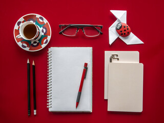 Overhead view of a desk. Red table and objects arranged in an orderly manner. Notebooks, pencils,...