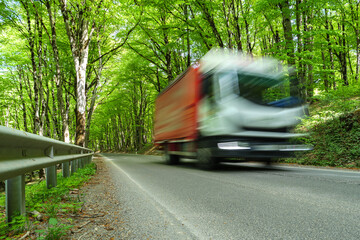 A red and white truck drives quickly along a winding road through a lush green forest, blurred by...