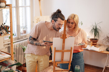 Focused artistic couple painting together on easel at creative art studio