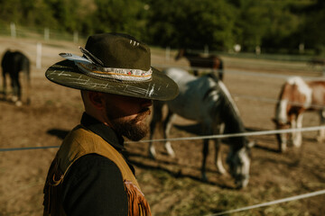 Side view of rancher with hat at ranch with horses grazing grass.