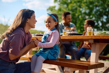 Happy girl talking to her mother during family picnic in nature.