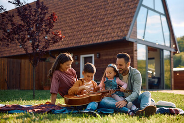 Happy family enjoying in camping day while boy is playing acoustic guitar.