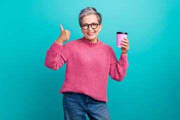 Photo of positive person with gray hair dressed knit sweater in eyewear hold cup of latte show...