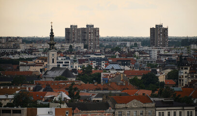 Fototapeta premium Serbia - Beautiful Panoramic view of Novi Sad and Danube River, spring cloudy evening. Red tiled roofs of houses and church towers with clocks. View from Petrovaradin fortress.