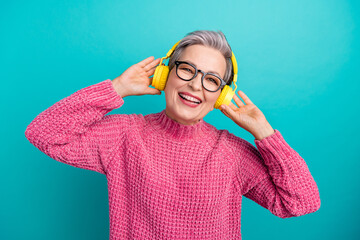 Photo of satisfied woman with short hair dressed pink sweater in glasses touching headphones emjoy...