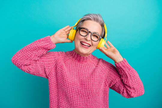 Photo of satisfied woman with short hair dressed pink sweater in glasses touching headphones emjoy music isolated on teal color background