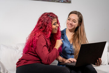 Par de amigas viendo e interactuando con su laptop. Hablando en el sofá de su casa