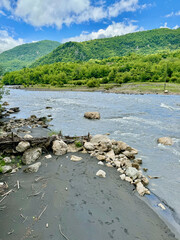 A view of the river with an muddy bank and green mountains with trees under sky near Kinchkha Canyon in Georgia 
