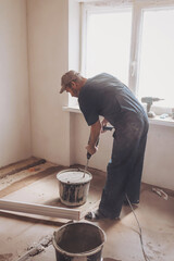 Male builder in work overalls kneading a solution using a construction perforator for plastering.