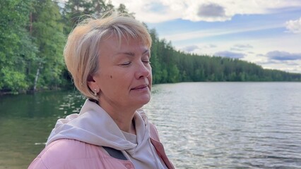 Beautiful old woman dreaming and meditation outdoors near lake in nature