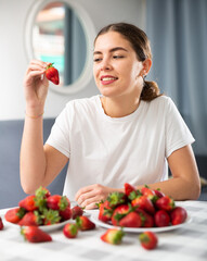 Portrait of a happy woman with strawberries at the table in the room at home