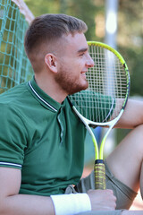 Young happy handsome man in polo play tennis outdoors with tennis racket on court at summer day