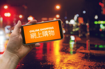 Online shopping, China import visualization. Hand holding a phone with orange text "online shopping" representating a store market app. Same in Chinese language. Colorful city lights in background. 