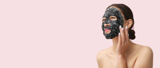 Young woman with activated charcoal mask on her face against pink background