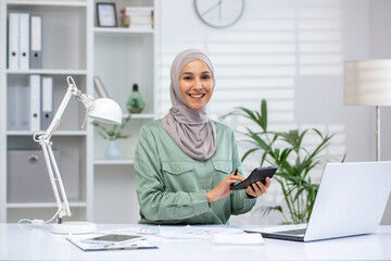 Portrait of successful and happy businesswoman financier, woman in hijab smiling and looking at...