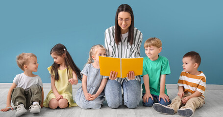 Little children with nursery teacher reading book near blue wall
