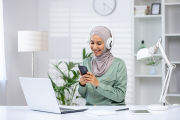 Young woman in hijab watching online video and listening to music, businesswoman at workplace...