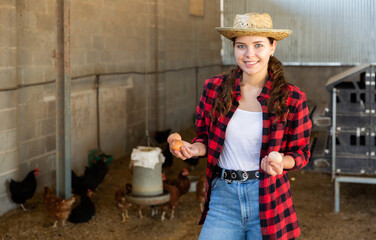 Portrait of happy young woman farmer standing in hen house with fresh chicken eggs in hands © JackF