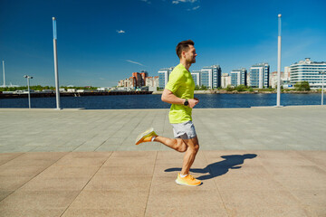 A man in a yellow shirt and shorts runs along a waterfront promenade on a sunny day, with modern...