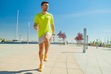 A man in a yellow shirt and shorts exercises outdoors on a sunny day in an urban park near the...