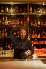 Young elegant barman working behind a bar counter mixing drinks